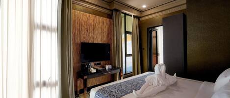A hotel room with a large bed, a flat-screen TV mounted on a wooden panel wall, a bedside table with a coffee maker, and a view of the outdoors through a window.