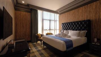 Een hotelkamer met een groot bed, een flatscreen televisie, een wand van houten panelen en een raam met gordijnen.