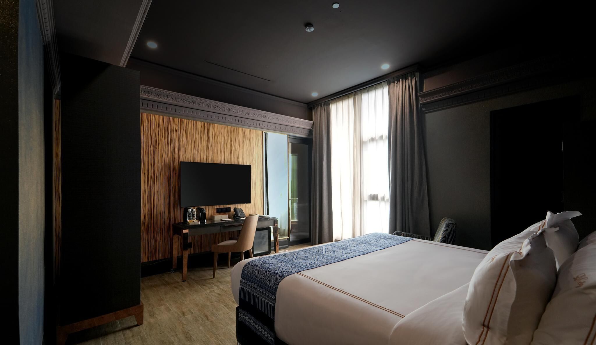 Habitación de hotel con una cama grande, un escritorio con computadora, un televisor de pantalla plana y un ventanal con cortinas.
