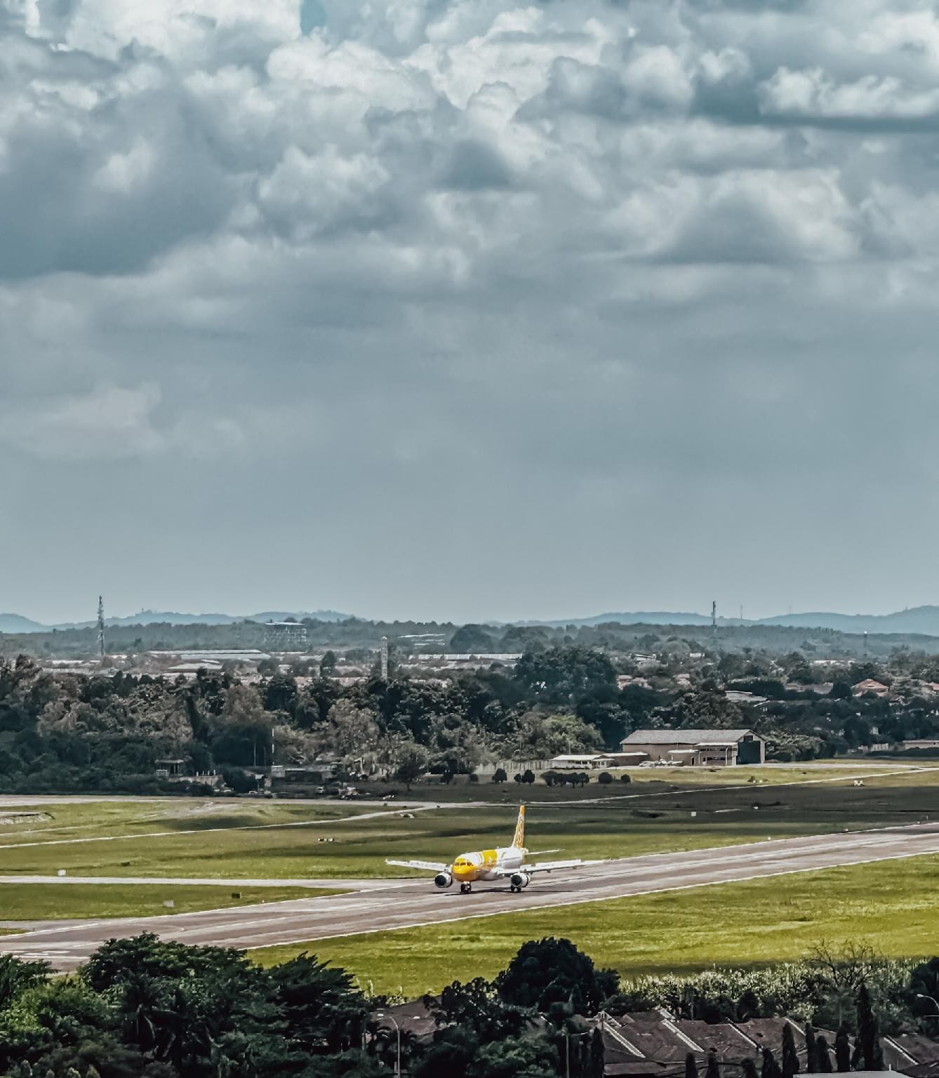An airplane on a runway with a backdrop of a cloudy sky and distant landscape.
