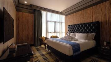 A hotel room with a large bed, a flat-screen TV, a wooden accent wall, and a window with curtains.