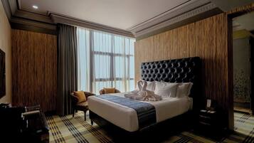 A hotel room with a large bed, a chair, a desk, and a large window.