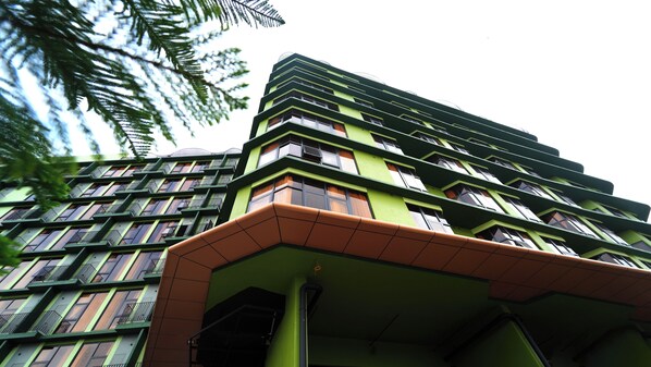Un edificio de varios pisos con una fachada distintiva verde y marrón, que cuenta con una serie de balcones y ventanas.