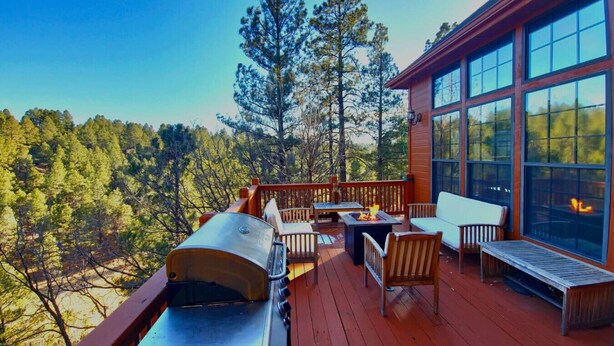 A wooden deck with outdoor furniture, a grill, and large windows overlooking a forest. - Upscale Family Mountain Cabin ~Deck w/ views + Fire Table ~Game Room (Flagstaff)