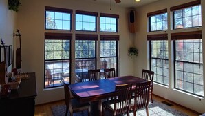 A dining area with a large table, chairs, and a ceiling fan. There are multiple windows providing natural light and views of the outdoors. - Upscale Family Mountain Cabin ~Deck w/ views + Fire Table ~Game Room (Flagstaff)