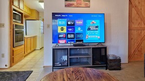 Ein Wohnzimmer mit Fernseher, der verschiedene Streaming-Dienste anzeigt, einem Holzschrank und Blick auf die Küche.