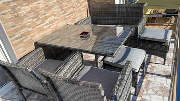 Un patio con mobiliario de mimbre, una mesa de vidrio y un muro de ladrillo.