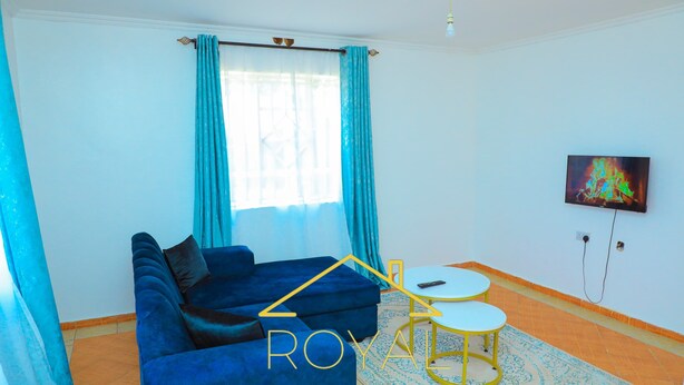 A room with a blue sofa, a small white table, and a TV on the wall.