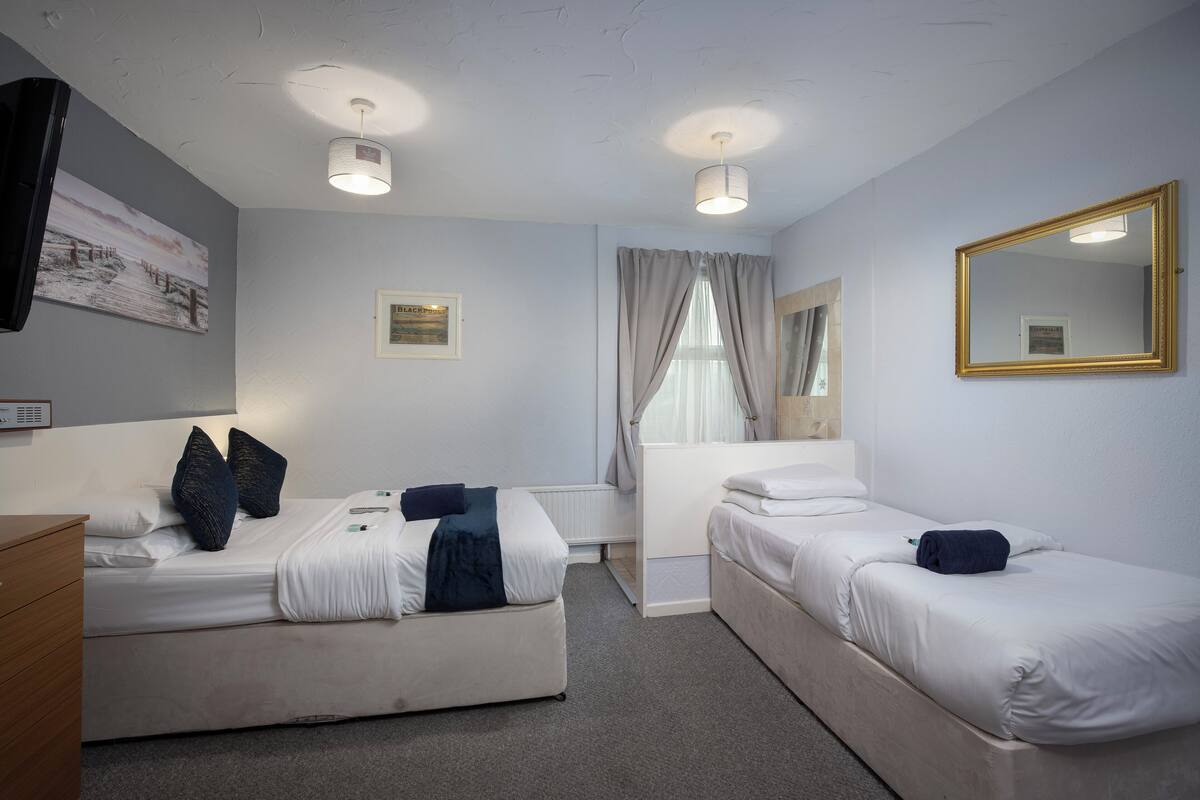 Hotellihuone, jossa on kaksi sänkyä, työpöytä, tuoli, peili ja taulu seinällä.