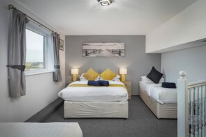 Ett hotellrum med en stor säng, en mindre säng, två sängbord med lampor, ett fönster med gardiner och en tavla på väggen.