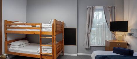 Une chambre avec un lit superposé, un lit simple, une télévision, une table de chevet et une fenêtre avec des rideaux.