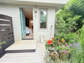 A wooden deck leading to a bedroom with a window, a door, and a shower area. - Cozy & Charming Studio Apartment on Folly Beach (Folly Beach)
