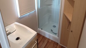 A compact bathroom with a glass shower enclosure, a sink, and wooden flooring. - Smart Home Venezia EP Rulantica 15min (Boofzheim)