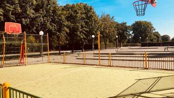 An outdoor basketball court with a fence, trees, and a clear sky.