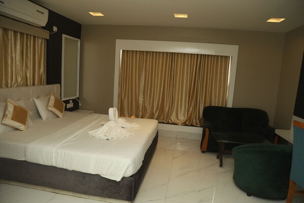 Quarto de hotel com uma cama grande, uma cadeira, uma mesa e uma janela com cortinas.