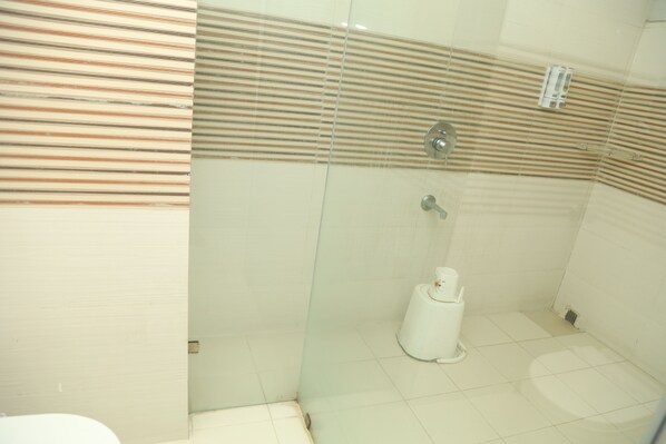 A bathroom with a glass partition, a toilet, and a shower area. - Geetanjali International (Deoghar)