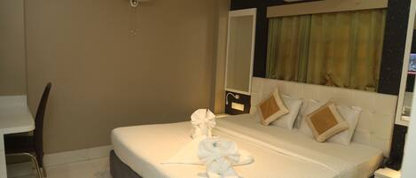 A hotel room with a bed, a desk, a chair, a ceiling fan, and an air conditioning unit.