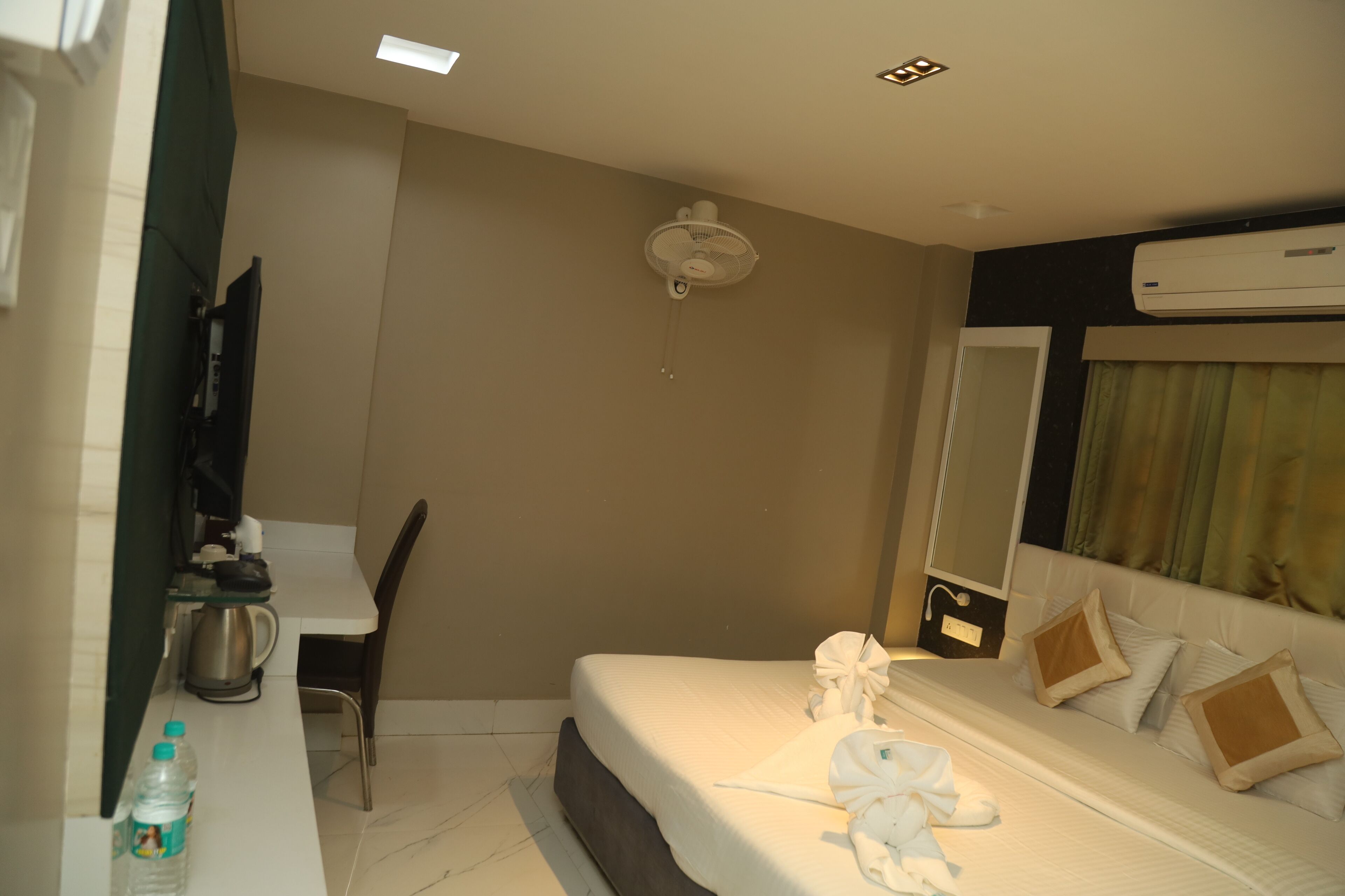 A hotel room with a bed, a desk with a coffee maker, a bottle of water, and an air conditioner.
