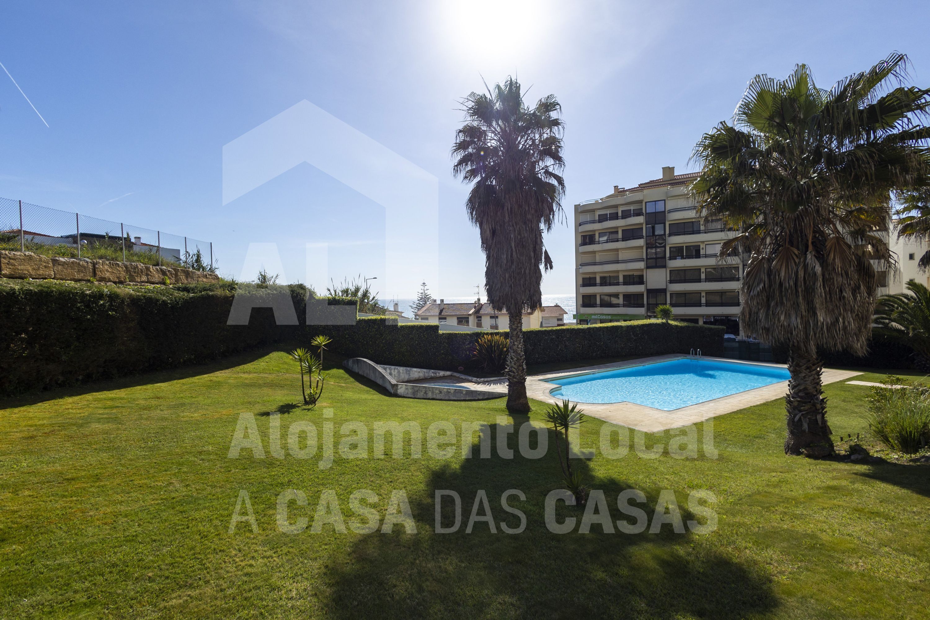 A well-maintained outdoor area with a swimming pool, palm trees, and a building in the background.