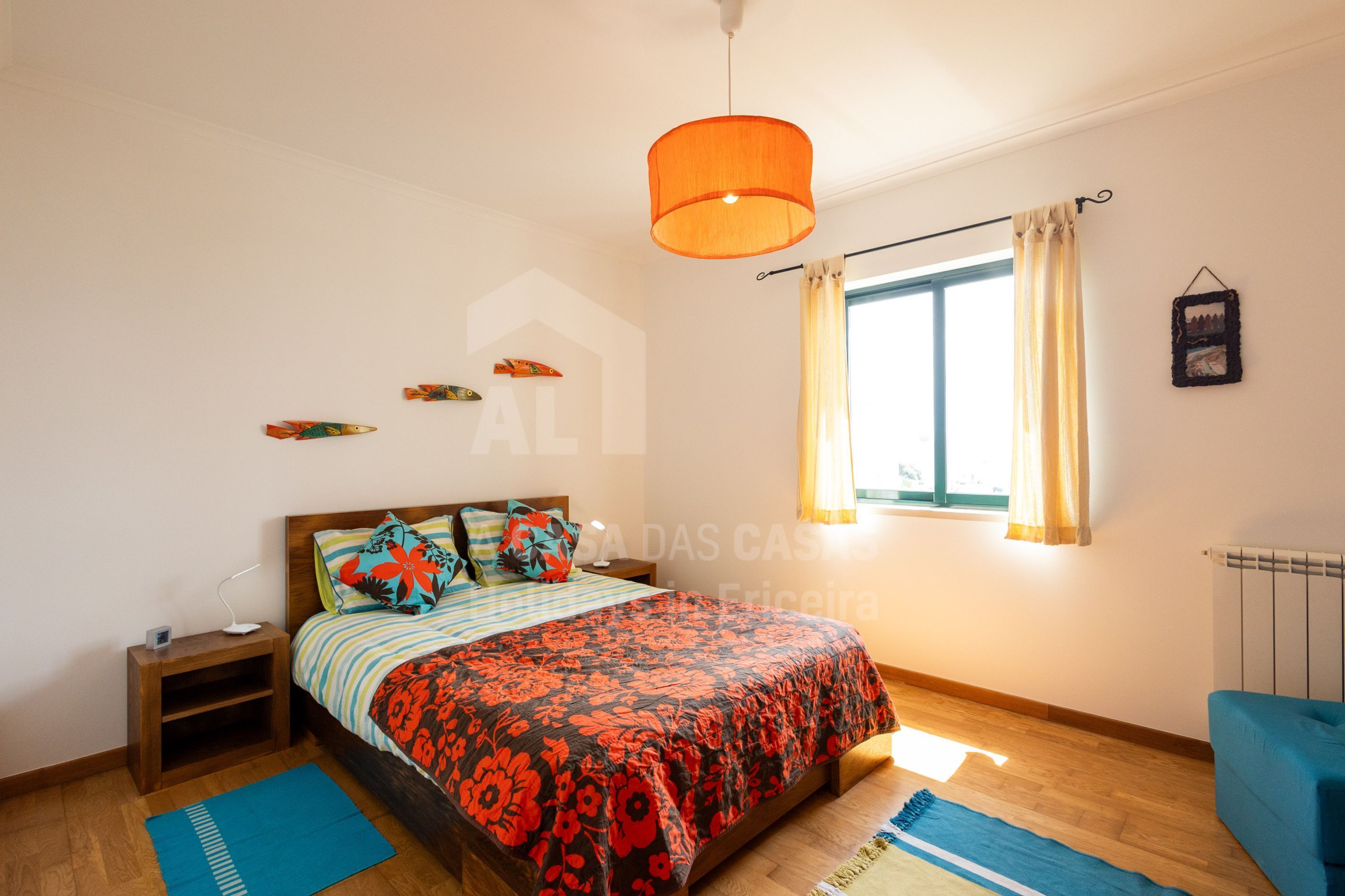 A bedroom with a bed, a nightstand, a window with curtains, and a hanging picture.