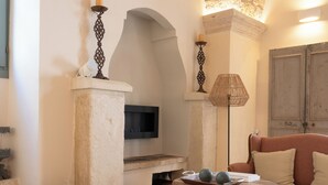 Un salon chaleureux avec un plafond en pierre, un canapé en bois, une table ronde sur laquelle est disposée une corbeille de fruits, et un téléviseur fixé au mur.