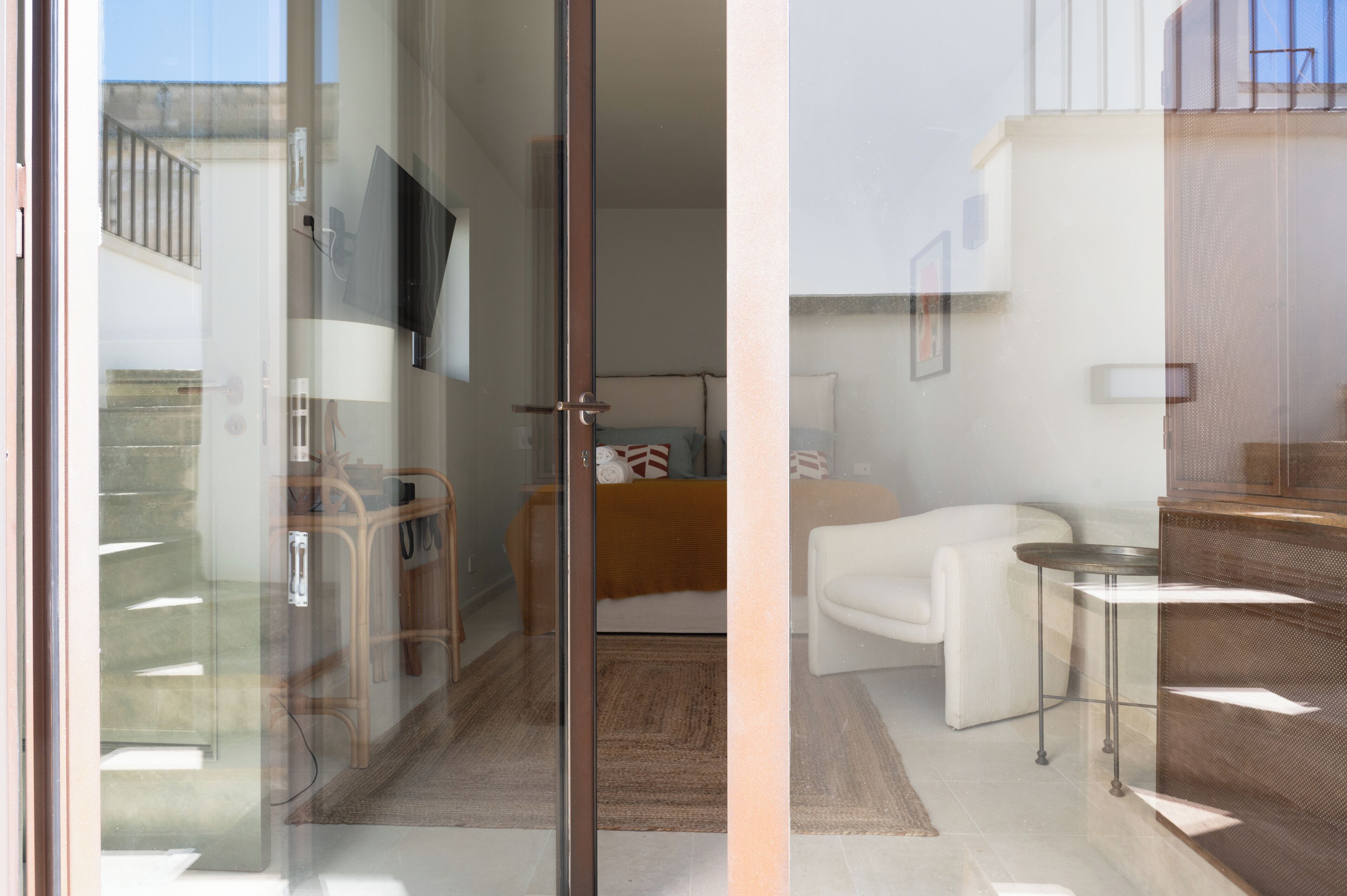 Un interior moderno con un vidrio corredizo que da a un balcón, un sofá, una mesita y un televisor montado en la pared.