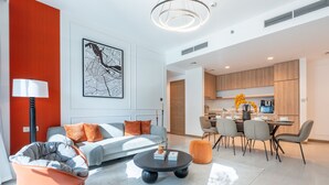 Un salon moderne avec un canapé, une table basse et un pouf orange. On y trouve également un coin repas avec une table et des chaises.