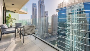 Un balcon avec vue sur les immeubles de grande hauteur, un coin salon avec une chaise et une petite table, et une plante en pot.