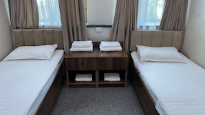 A hotel room with two single beds, a wooden nightstand with towels, and a window with curtains. - Qorasuv hotel (Tashkent)