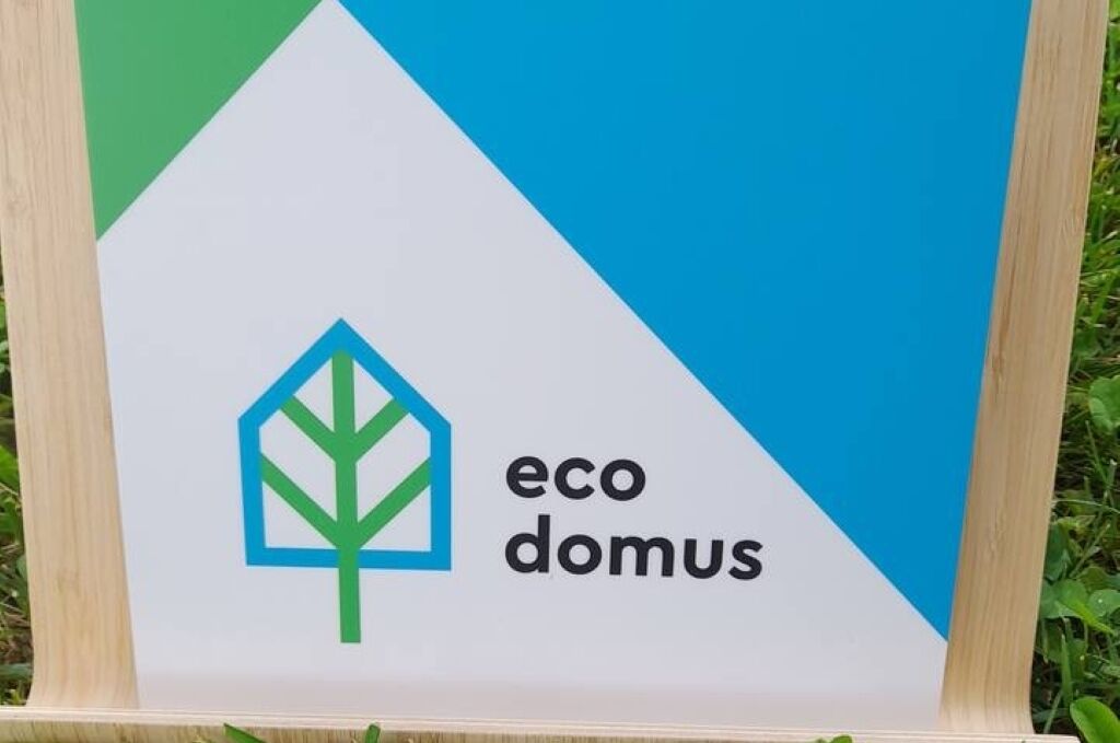 A sign with the logo and name "eco domus" on a white background with a blue and green design.