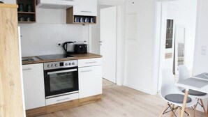 Moderni keittiö, jossa on valkoiset kaapit, sisäänrakennettu uuni ja liesi. Keittiössä on myös ruokailutila, jossa on valkoinen pöytä ja tuolit.