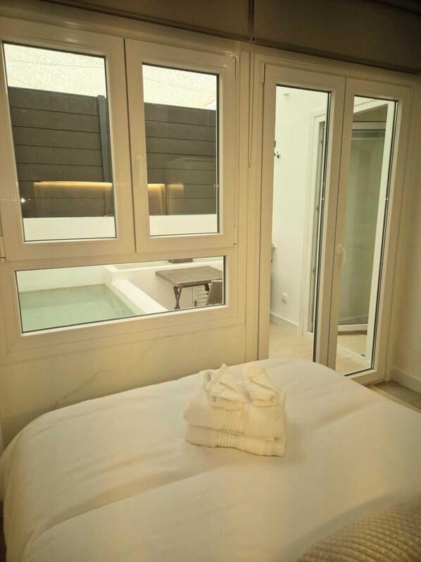Un dormitorio con cama, ventana con vista a una terraza de madera y puerta corrediza que da a un baño.