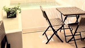 A sunlit patio area with a hot tub, two wicker chairs, and a small potted plant.