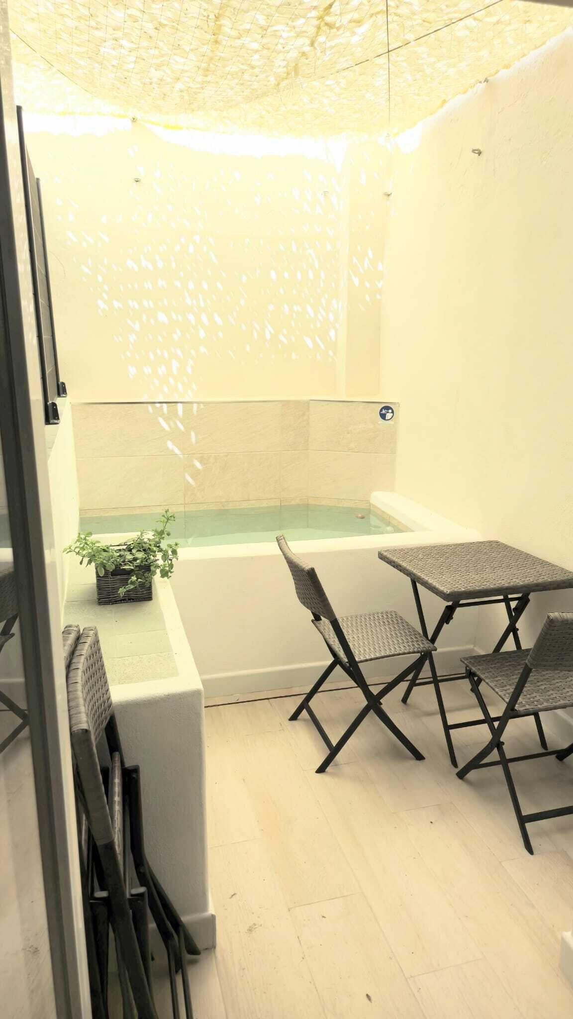 Un espacio exterior pequeño y cerrado con un jacuzzi, dos sillas plegables y una mesita.