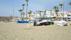 A beach with several boats, palm trees, and a row of buildings in the background.