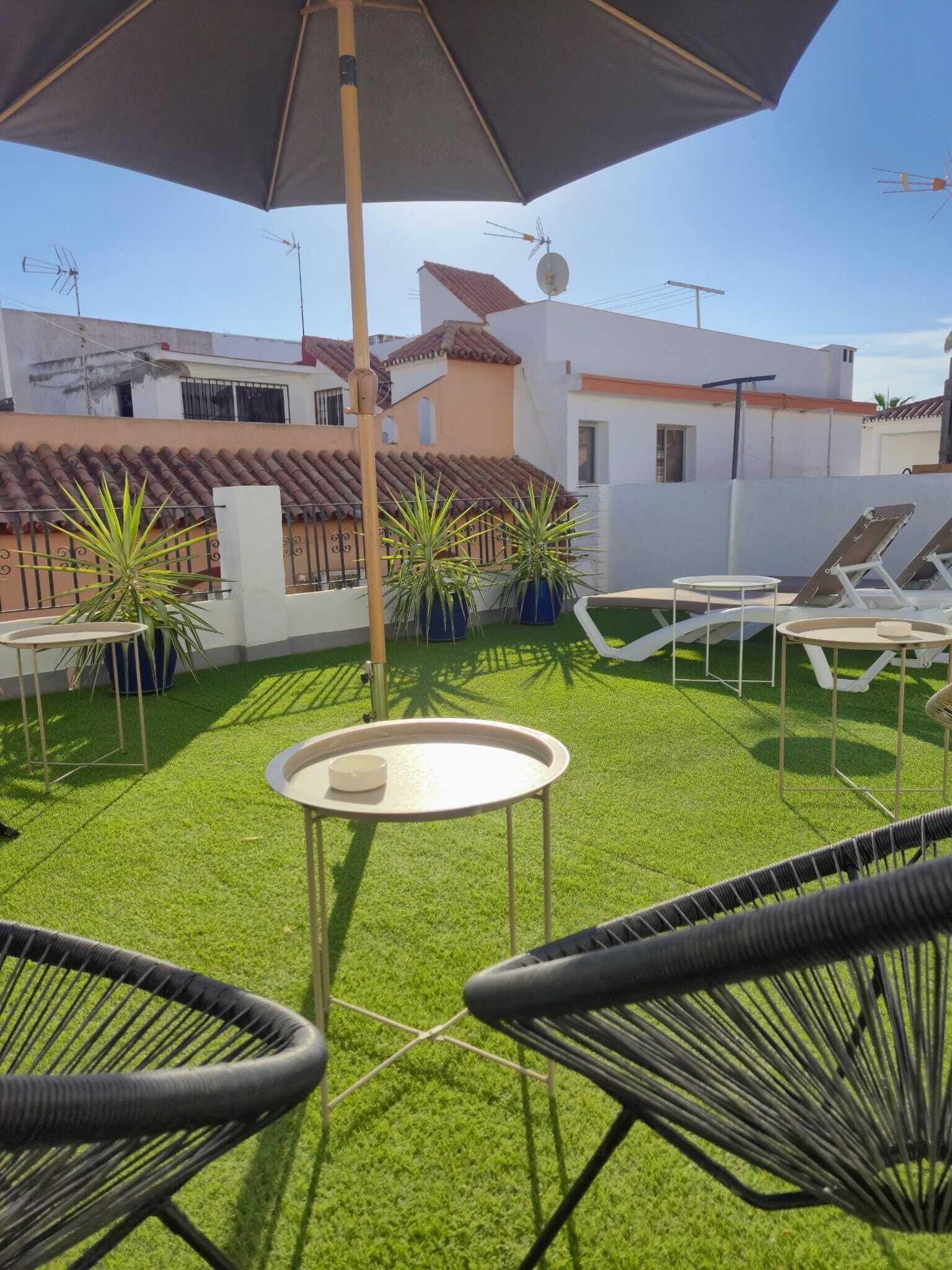 Un patio con césped artificial, sillones de descanso y una mesa.