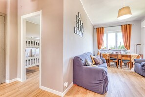 Un saló modern amb un sofà gris, una taula de menjador amb cortines taronja, i una escala que porta a un balcó.