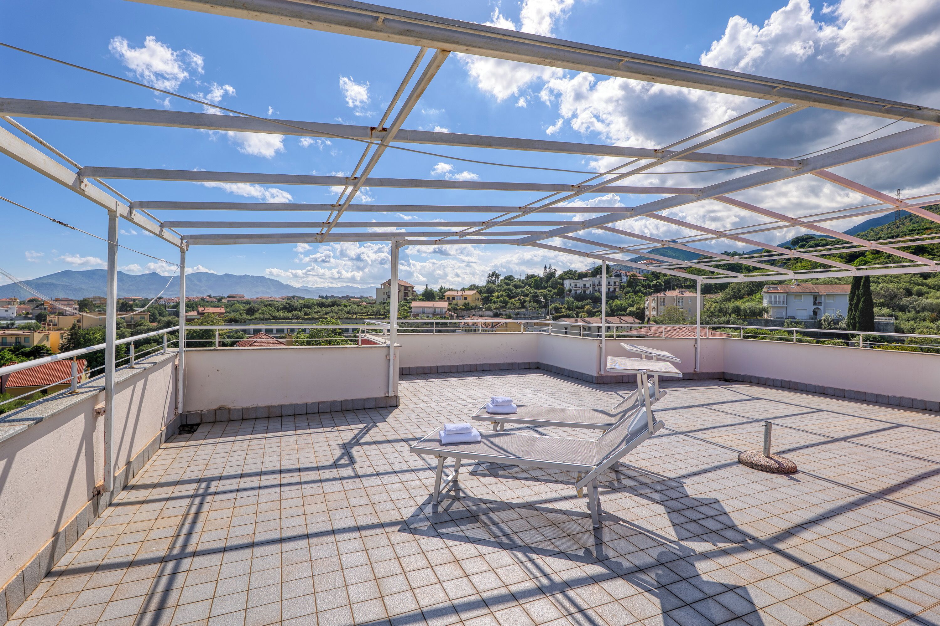 Une terrasse sur le toit dotée d’une structure métallique, d’un sol carrelé et offrant une vue sur les montagnes et les bâtiments situés au loin.