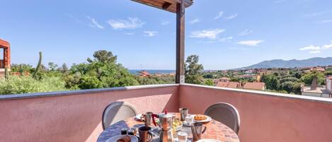 A round table with chairs on a balcony overlooking a scenic landscape with mountains and a clear sky.