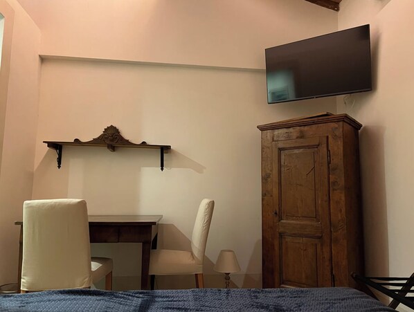 Un dormitorio con cama, escritorio, silla, televisión montada en la pared y armario de madera.