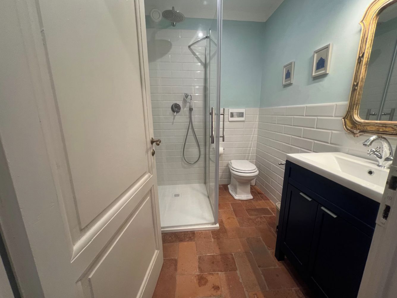 Een badkamer met een douchecabine van glas, een wit toilet en een donkerdressoir met een wastafel.