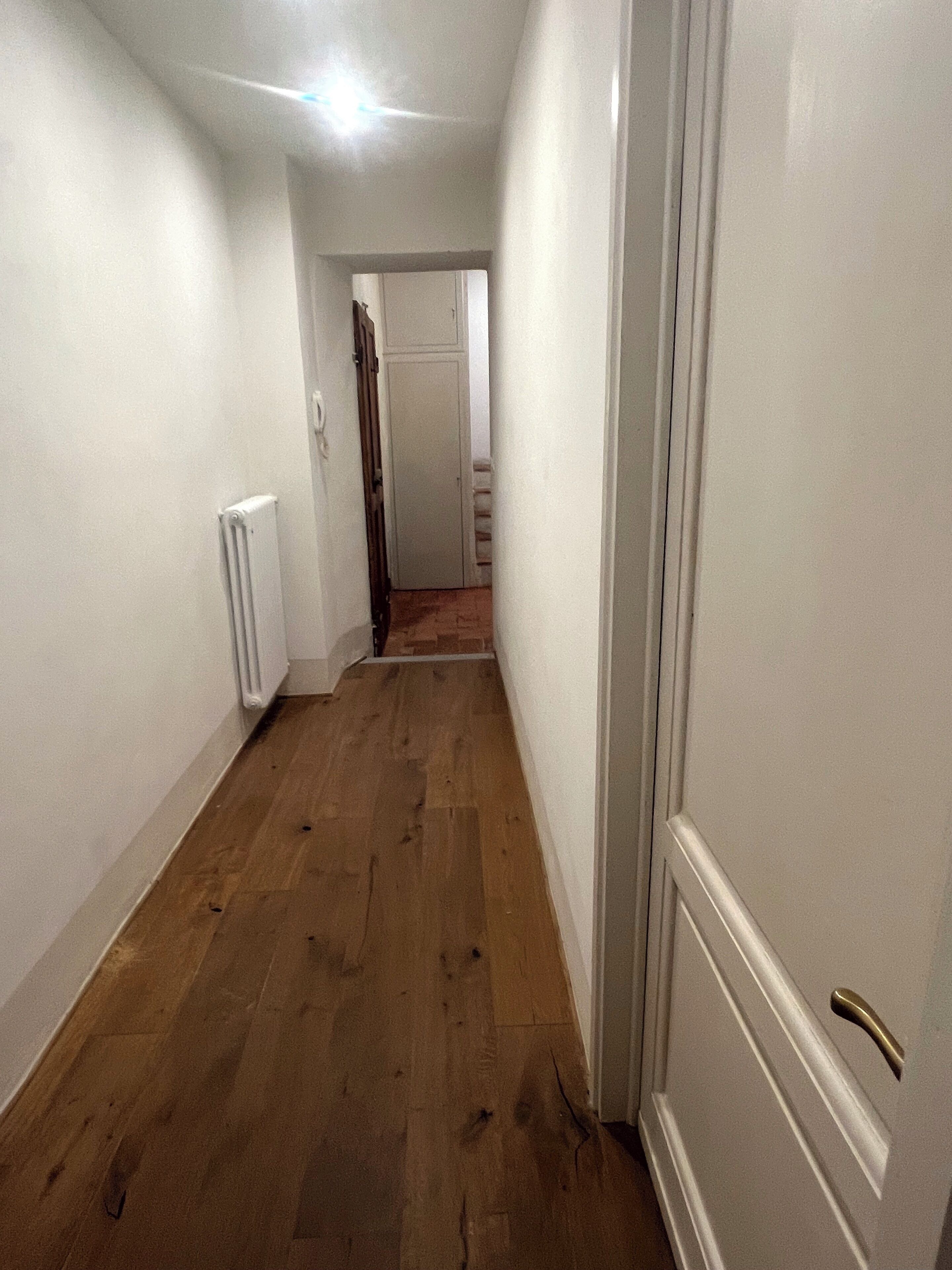 Un pasillo estrecho con piso de madera y paredes blancas.