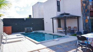 A modern outdoor pool area with a pergola, lounge chairs, and a dining table with chairs.