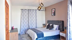 A bedroom with a bed, curtains, a bedside table, and a wall-mounted air conditioner.