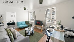 Un salon moderne avec un canapé gris, un fauteuil bleu, une table basse et un coin repas avec une table mise pour deux personnes.