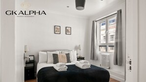 Une chambre d’hôtel moderne avec un lit bien fait, une petite table de chevet avec une lampe et une fenêtre avec des rideaux.