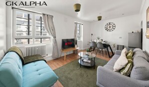 Una sala de estar moderna con sofá, televisor, comedor y un reloj en la pared.