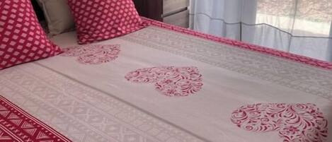 Une chambre à coucher avec un lit, des oreillers, une commode et une fenêtre avec des rideaux.