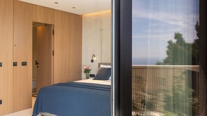 Un dormitorio moderno con una cama grande, un armario de madera y vistas a la vegetación desde un balcón.