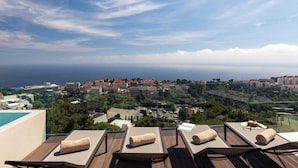 Terraza en la azotea con tumbonas y piscina, con vistas a un pueblo costero y al mar.